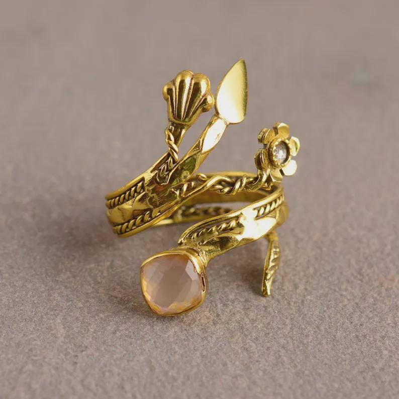 Peut inclure: Une bague dor&eacute;e au design unique. La bague est orn&eacute;e d'une pierre pr&eacute;cieuse rose p&acirc;le et de d&eacute;tails floraux et en forme de coquillage. La bague s'enroule autour du doigt et a une apparence d&eacute;corative et artistique.