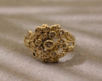Könnte beinhalten: Ein goldfarbener Ring mit floralem Design. Der Ring zeigt eine Ansammlung detaillierter Blumen und Blätter, die ein zartes und verziertes Aussehen erzeugen. Das Design des Rings ist aufwendig, wobei jedes Blütenblatt und jedes Blatt klar definiert ist.