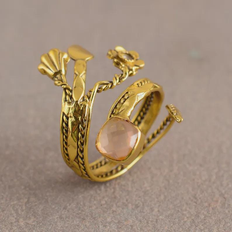 Peut inclure: Une bague dor&eacute;e avec un motif floral et de feuilles. La bague pr&eacute;sente une pierre pr&eacute;cieuse rose clair de coupe carr&eacute;e. La bande a un motif tress&eacute; textur&eacute;. La bague a un design ouvert unique.