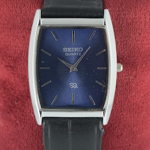 Könnte beinhalten: Eine rechteckige Seiko Quartz-Uhr mit dunkelblauem Zifferblatt und silberfarbenem Gehäuse. Die Uhr hat ein schwarzes Lederarmband und eine kleine Krone an der Seite. Das Zifferblatt zeigt das Seiko-Logo und das SQ-Symbol.