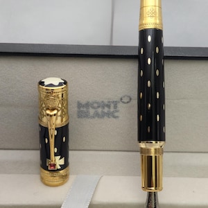May include: A black and gold Montblanc fountain pen with a polka dot design. The pen features gold accents, a detailed nib, and a decorative cap. The pen is displayed in its original box with the Montblanc logo.