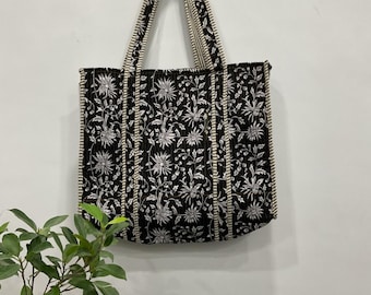 Può includere: Borsa tote nera con un motivo floreale bianco. La borsa ha manici lunghi e strisce verticali color crema. La borsa è appesa a una parete bianca.
