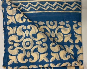 May include: Folded blue and cream fabric with a repeating pattern. The fabric has a cream border and a central design of blue and cream floral and geometric shapes. The fabric is folded, showing the pattern on the top layer.
