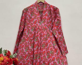 May include: A long-sleeved dress featuring a vibrant pink background with a repeating pattern of red tomatoes and green stems. The garment has a V-neckline, a structured collar, and a gathered waistline that flows into a full, pleated skirt.