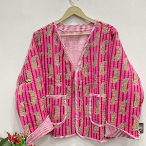 Pode incluir: Um casaco acolchoado com um padrão de riscas verticais em rosa vibrante e vermelho escuro com um motivo de leopardo repetido. O casaco tem um decote em V, mangas compridas com punhos dobrados e dois bolsos frontais, com acabamento em riscas brancas e cor-de-rosa.