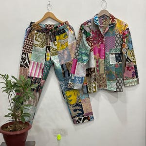 May include: A colourful patchwork pajama set, comprising a button-down shirt and drawstring trousers. The set displays a variety of fabric patterns in pink, blue, yellow, and green. The shirt and trousers are suspended on wooden hangers.
