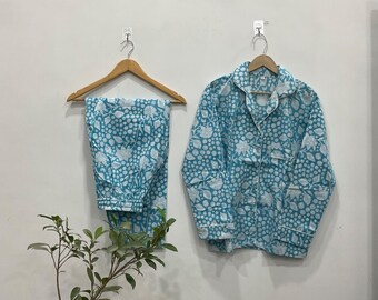 May include: A light blue and white floral patterned pajama set. The set comprises a button-down shirt and matching trousers, both hanging on wooden hangers. The pajamas are made of a soft fabric and have a relaxed fit. The set is displayed against a white wall.