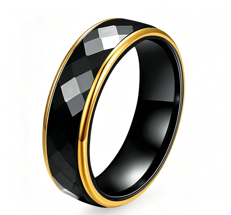 Op de afbeelding: Een zwarte ring met een facet, geometrisch ontwerp. De ring heeft een goudkleurige band aan de boven- en onderranden. De ring staat tegen een witte achtergrond.
