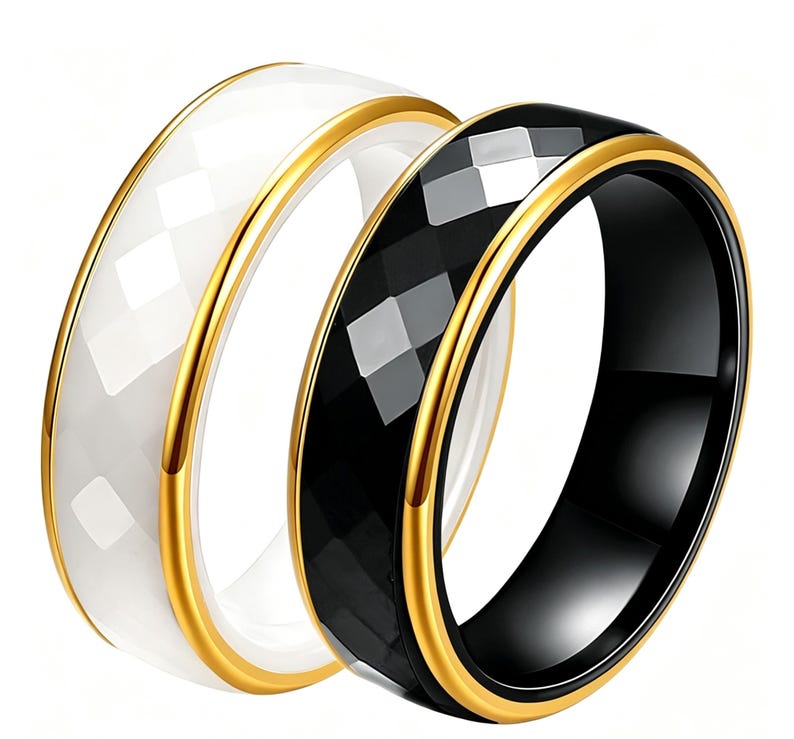 Op de afbeelding: Twee ringen, &eacute;&eacute;n wit en &eacute;&eacute;n zwart, met een facetontwerp. Beide ringen hebben een goudkleurige band langs de randen. De witte ring staat links en de zwarte ring rechts. De ringen staan tegen een witte achtergrond.