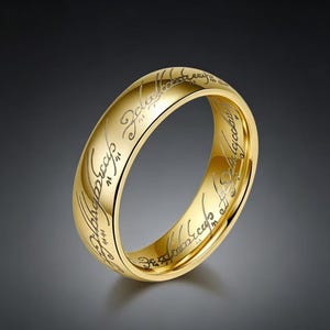 May include: A gold-coloured ring with engraved script around the band. The ring has a polished finish and a classic design. The engraved text is in a stylized font. The ring is likely made of metal and is a piece of jewellery.