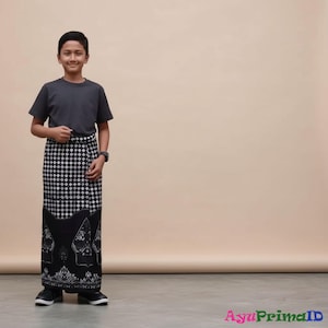 以下が含まれることがあります： 濃いグレーのTシャツと、白と黒の模様のサロンを身に着けた人。サロンは上部に幾何学模様、下部に詳細なイラストが施されています。その人は黒い靴も履いています。