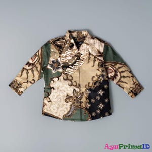 Könnte beinhalten: Ein langärmliges Hemd mit Batikmuster. Das Hemd zeigt eine Mischung aus Farben, darunter Olivgrün, Schwarz und Beige, mit floralen und geometrischen Designs. Das Hemd hat einen Kragen und ist aus leichtem Stoff gefertigt.