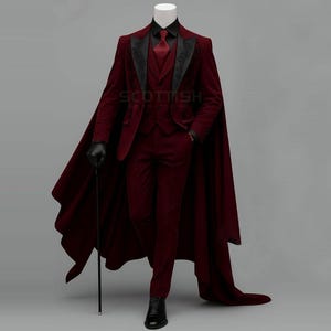 May include: A deep burgundy suit featuring a matching cape, a waistcoat, and trousers. The jacket has black lapels with intricate embroidery, paired with a black shirt and a burgundy tie. A black cane is held in one hand, and black shoes are worn.