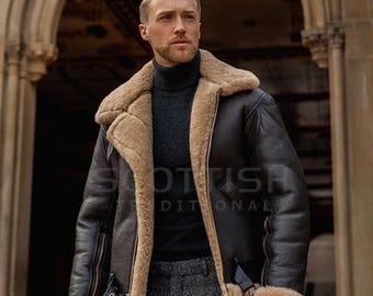 Può includere: Giacca in pelle marrone scuro con fodera e colletto in montone beige. La giacca ha un classico stile aviatore con cinturino con fibbia e chiusura con cerniera. Il testo "SCOTTISH TRADITIONAL" è visibile.