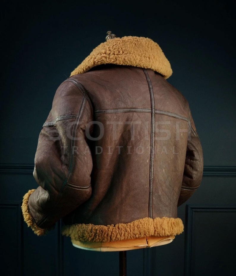 Pu&ograve; includere: Giacca in pelle marrone con colletto e finiture in montone beige. La giacca ha un design classico con la schiena cucita a croce e il testo "SCOTTISH TRADITIONAL" nella parte inferiore.