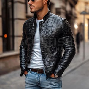 Könnte beinhalten: Schwarze Lederjacke mit Krokodilhautstruktur. Die Jacke hat einen Stehkragen und einen Reißverschluss. Die Person trägt ein weißes T-Shirt und eine blaue Jeans. Ein brauner Gürtel und eine Uhr sind ebenfalls sichtbar.