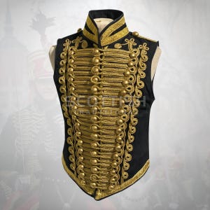 Puede incluir: Chaleco negro con ribetes dorados y elaborados detalles de cuerda y botones dorados. El chaleco tiene un cuello alto y probablemente forma parte de un disfraz militar o histórico. El chaleco se exhibe en un maniquí.