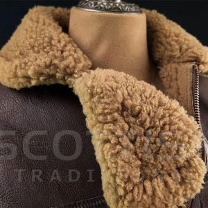 Pu&ograve; includere: Giacca in pelle marrone con colletto e fodera in montone. La giacca ha una chiusura con cerniera e il testo "SCOT TRADI" &egrave; impresso sulla pelle. La giacca &egrave; esposta su un manichino.