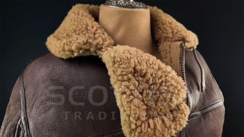 Pu&ograve; includere: Giacca in pelle marrone con colletto e fodera in montone. La giacca ha una chiusura con cerniera e il testo "SCOT TRADI" &egrave; impresso sulla pelle. La giacca &egrave; esposta su un manichino.