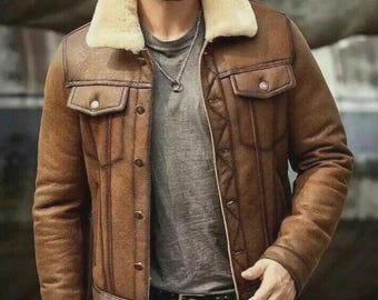 May include: A brown leather jacket with a cream-colored shearling collar. The jacket has two chest pockets with button closures and a button-up front. The jacket is worn with a gray t-shirt and a black belt.