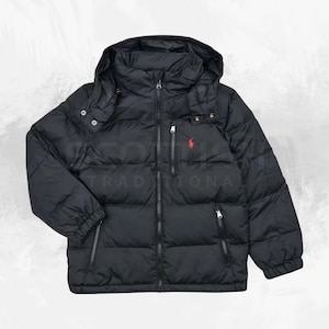 Puede incluir: Chaqueta acolchada negra con capucha, cierre de cremallera completo, dos bolsillos laterales y un pequeño logotipo rojo en el pecho. La chaqueta tiene un diseño acolchado y un aspecto cálido y aislado.