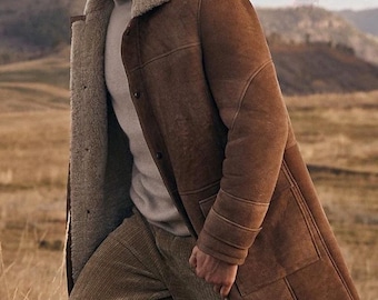 Può includere: Un cappotto in montone marrone con fodera in montone colorata e colletto a revers. Il cappotto è abbottonato e indossato sopra un dolcevita grigio chiaro e pantaloni di velluto a coste marroni. Lo sfondo presenta un campo e montagne.