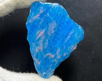 Może przedstawiać: Żywy niebieski okaz minerału z różowymi smugami. Surowy kamień jest trzymany przez rękę w rękawicy, ukazując jego naturalną teksturę i wariacje kolorystyczne. Kamień szlachetny ma krystaliczną strukturę.