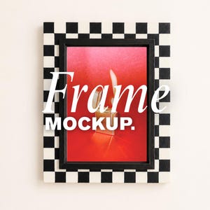 Può includere: Una cornice rettangolare con un bordo a scacchi bianco e nero. All'interno della cornice c'è una stampa che mostra un accendino metallico con una fiamma visibile su uno sfondo rosso vibrante, con il testo Frame MOCKUP.