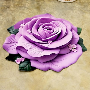 May include: A large, three-dimensional purple rose-shaped rug. The rug features layered petals in varying shades of purple, with small pink flower accents and green leaves. The rug is designed to resemble a realistic rose.