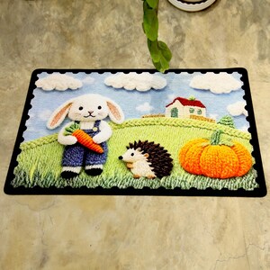 May include: A rectangular rug with a charming, embroidered design. It depicts a white rabbit in blue dungarees holding a carrot, a hedgehog, and a pumpkin. A house and clouds are in the background, set on a green field with a blue sky.