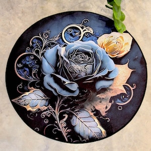 May include: A circular, dark blue decorative item with a large, stylized blue rose and a smaller yellow rose. Intricate silver and gold floral details and leaves surround the roses. The design has a vintage, artistic aesthetic.