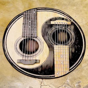 May include: Circular wall art depicting a yin-yang symbol formed by two acoustic guitars. One guitar is light-toned, the other dark, with strings and sound holes. The artwork is framed with a black border, creating a striking contrast.