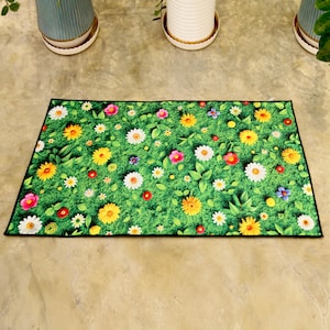 May include: A rectangular doormat with a green floral design. The mat showcases a dense pattern of colourful flowers, including yellow, white, pink, and red blooms, set against a backdrop of green grass and leaves. The mat is edged with a black trim.