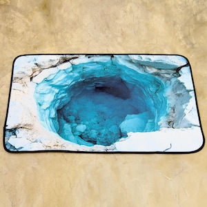 May include: Rectangular mouse mat featuring a vibrant image of a deep blue, water-filled cavern. The cavern is surrounded by white and grey rock formations, with a black border.