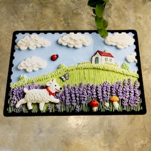 May include: A decorative rectangular mat with a charming landscape design. It depicts a white dog with a red collar, lavender fields, a small house, clouds, and a ladybug. The border is black.