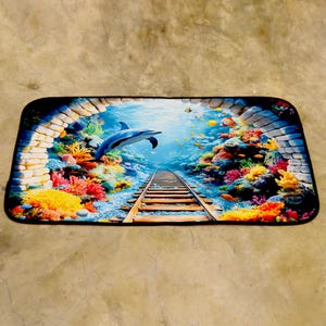 May include: Rectangular mat depicting an underwater scene with a blue dolphin. A railway track extends into the distance, surrounded by colourful coral and fish. The scene is framed by a brick archway. The mat has a black border.