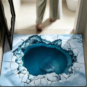 May include: A rectangular bath mat with a 3D ice cave design. The mat features a deep blue pool surrounded by cracked ice, creating an illusion of depth. The color palette includes shades of blue and white, with a person walking in the background.