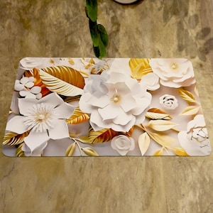 May include: Rectangular floral mat featuring large white paper flowers with gold and brown leaves. The mat has a light grey background and is suitable for indoor use. The design is a 3D effect.