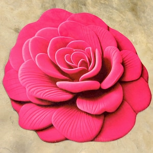 May include: A bright pink rug in the shape of a rose. The rug has detailed petal textures and a three-dimensional effect, creating a realistic floral design. The rug is a decorative accent piece, suitable for a living space.