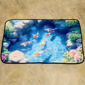 May include: Rectangular mat depicting a tranquil pond scene with koi carp. The design features a blue water background, rocks, and greenery with pink and purple flowers. The koi carp have orange, white, and black markings.