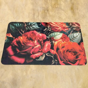 May include: Rectangular mat with a floral design of red roses and green leaves on a dark backdrop. The roses are depicted in full bloom, with detailed petals and varying shades of red. The mat has rounded edges.