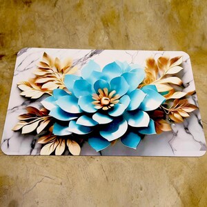 May include: A rectangular decorative item with a large, layered blue flower and a golden center. Gold and bronze leaves and a marble-effect background are also present. Likely for home decor, the item is rectangular in shape.