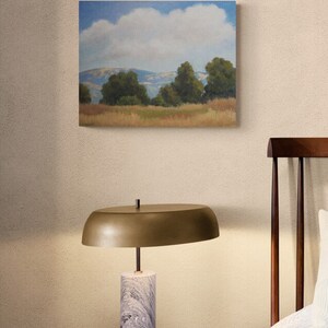 K&ouml;nnte beinhalten: Ein Gem&auml;lde einer Landschaft mit einer gro&szlig;en, flauschigen wei&szlig;en Wolke am Himmel. Die Landschaft zeigt sanfte H&uuml;gel, gr&uuml;ne B&auml;ume und ein Feld mit trockenem Gras.