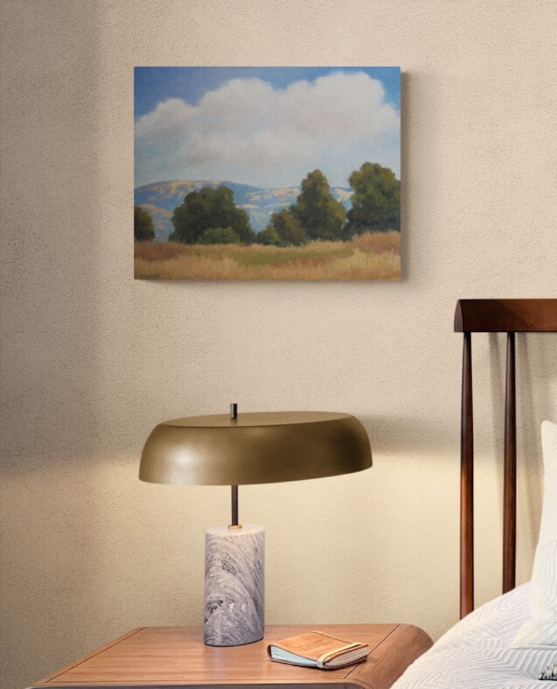 K&ouml;nnte beinhalten: Ein Gem&auml;lde einer Landschaft mit einer gro&szlig;en, flauschigen wei&szlig;en Wolke am Himmel. Die Landschaft zeigt sanfte H&uuml;gel, gr&uuml;ne B&auml;ume und ein Feld mit trockenem Gras.