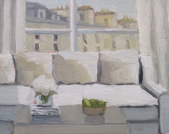 Puede incluir: Un sofá blanco con cuatro almohadas y una manta blanca. Un jarrón con flores blancas se encuentra en el sofá. Un tazón de fruta verde se encuentra en una mesa frente al sofá. El sofá está frente a una ventana con vista a una ciudad.