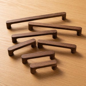 May include: A collection of six dark brown wooden cabinet handles of varying lengths. Each handle features a straight, rectangular bar design with rounded edges and two cylindrical mounting points, arranged in a staggered formation.