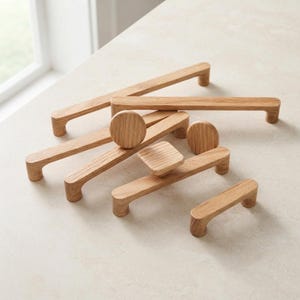May include: A collection of light brown wooden cabinet handles and knobs in various lengths and shapes. The set includes several long rectangular bar pulls, a circular knob, and a square knob, all featuring a smooth, natural wood grain finish.