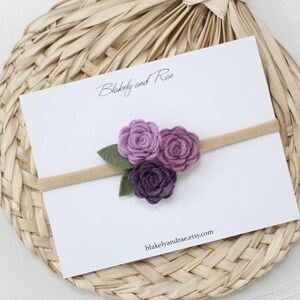 May include: A purple felt flower headband with three flowers and green leaves. The headband is on a white card with the text "Blakeely and Rae" and "blakeelyandrae.etsy.com".
