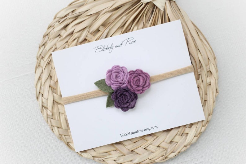 May include: A purple felt flower headband with three flowers and green leaves. The headband is on a white card with the text "Blakeely and Rae" and "blakeelyandrae.etsy.com".