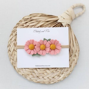 May include: A pink felt flower headband with three flowers and green leaves. The headband is on a white card with the text "Blakely and Rae" and "blakelyandrae.etsy.com".